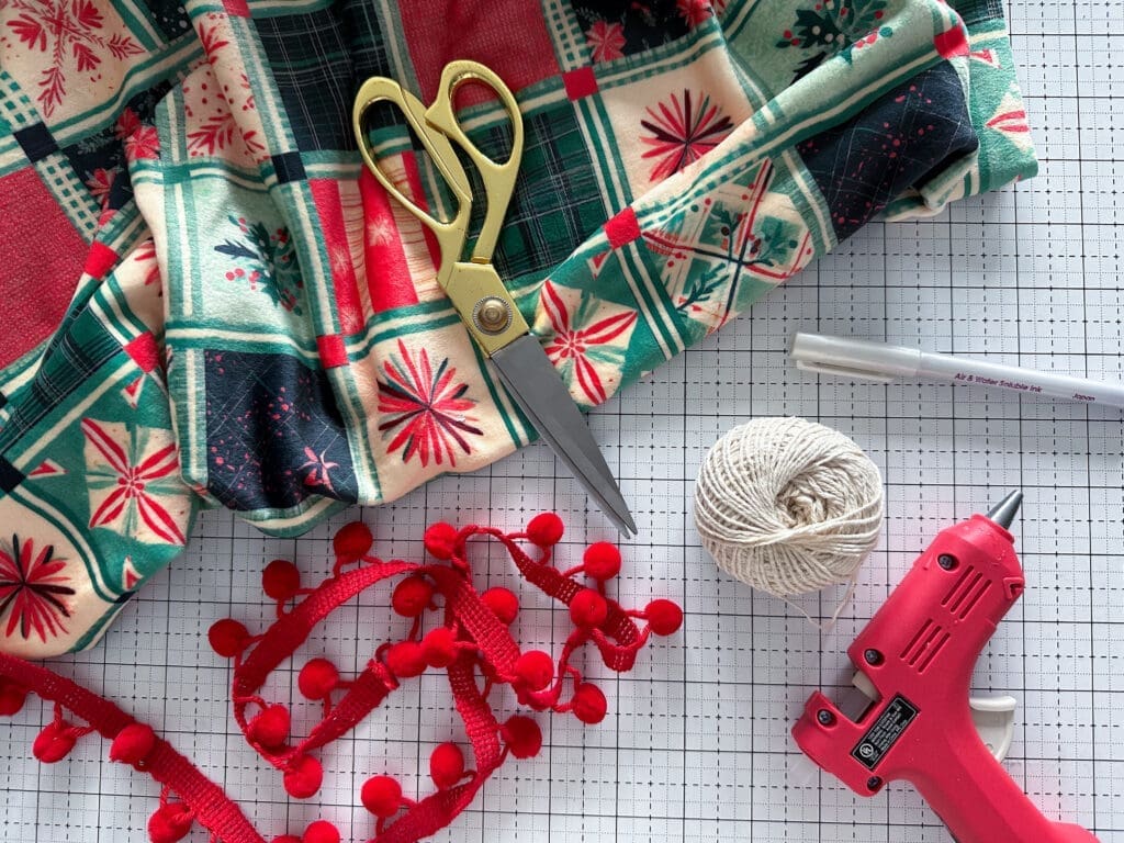 Supplies needed for the no sew christmas tree skirt, including fabric glue gun, and trim