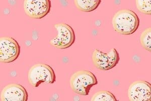 white frosted sprinkle sugar cookies with bites taken out of them, on a pink background with gold confetti.