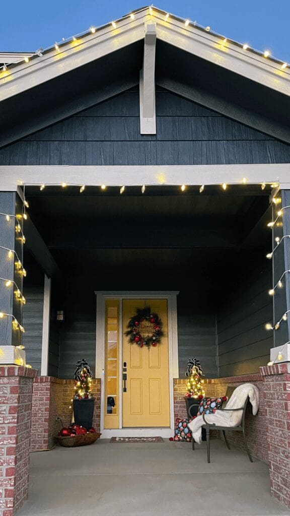 Welcoming front porch with bright yellow door, decorated for Christmas surrounded by warm white lights