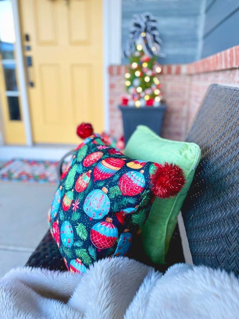 Nutcracker inspired porch pillow with traditionally colored hand painted ornaments and red glitter pom poms on the corners