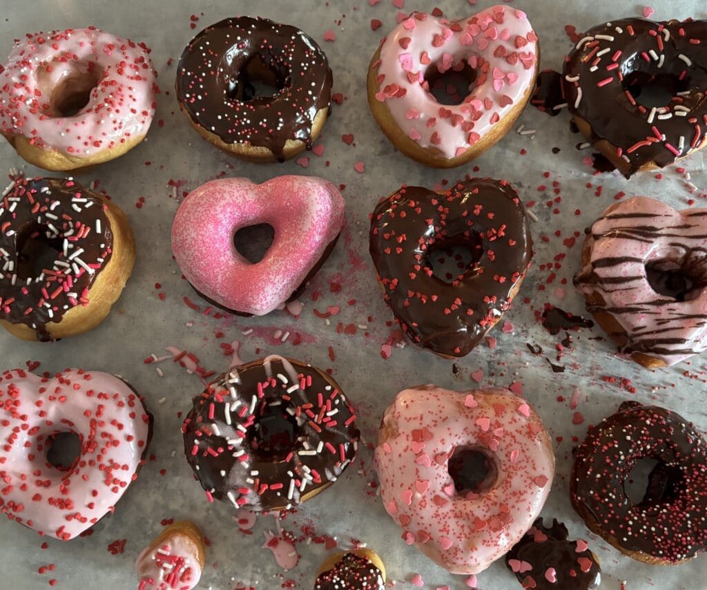 Valentine's day heart shaped donuts sitting on parchment paper, decorated