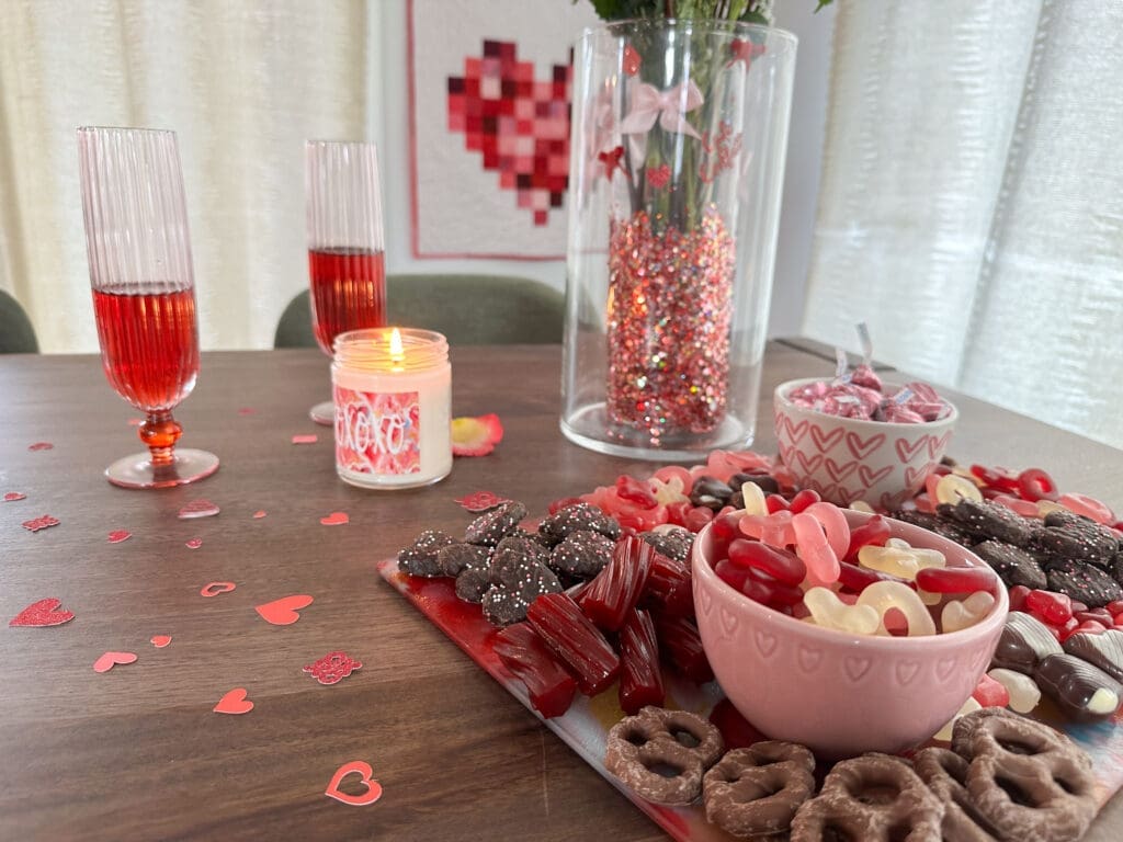 Pink and red valnetine's day table with snack board, candle, and glitter centerpiece