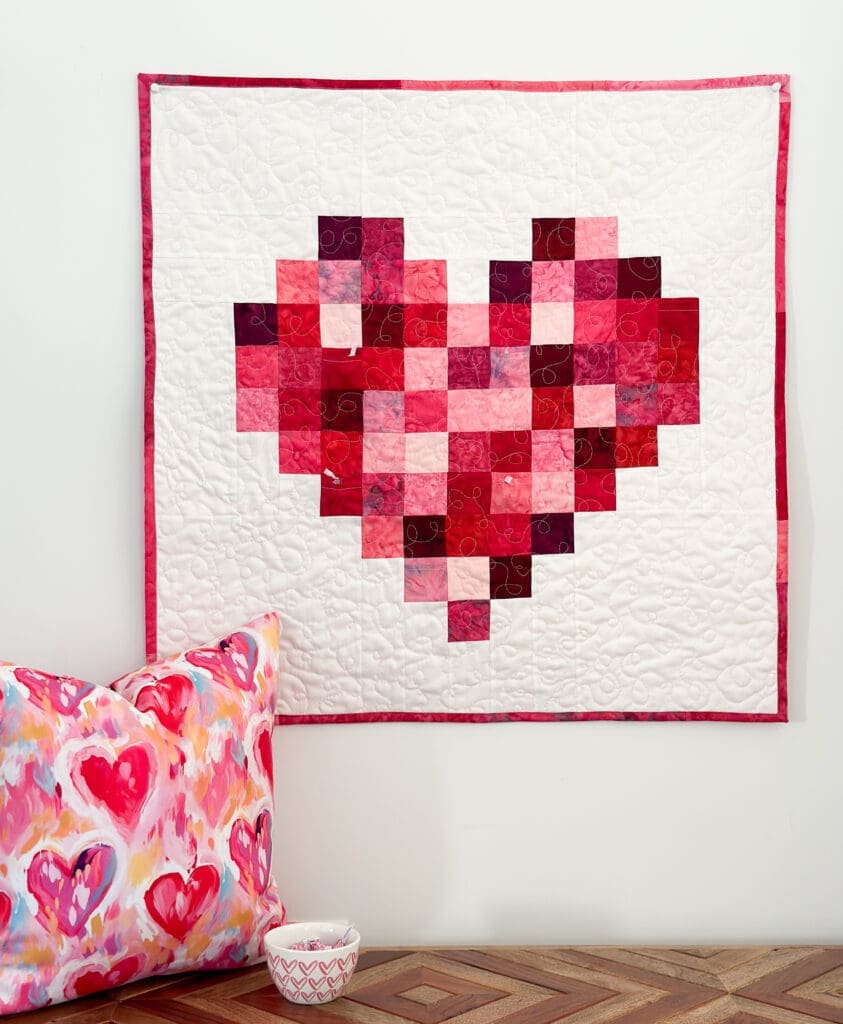 An example of creative living: Beautiful heart quilt hanging on wall above bench with matching painted hearts pillow by Zappy Dots and a bowl of candy.